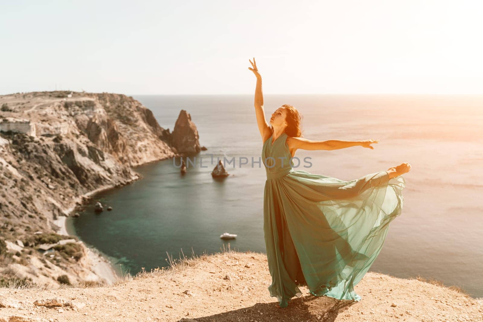 Woman green dress sea. Female dancer posing on a rocky outcrop high above the sea. Girl on the nature on blue sky background. Fashion photo