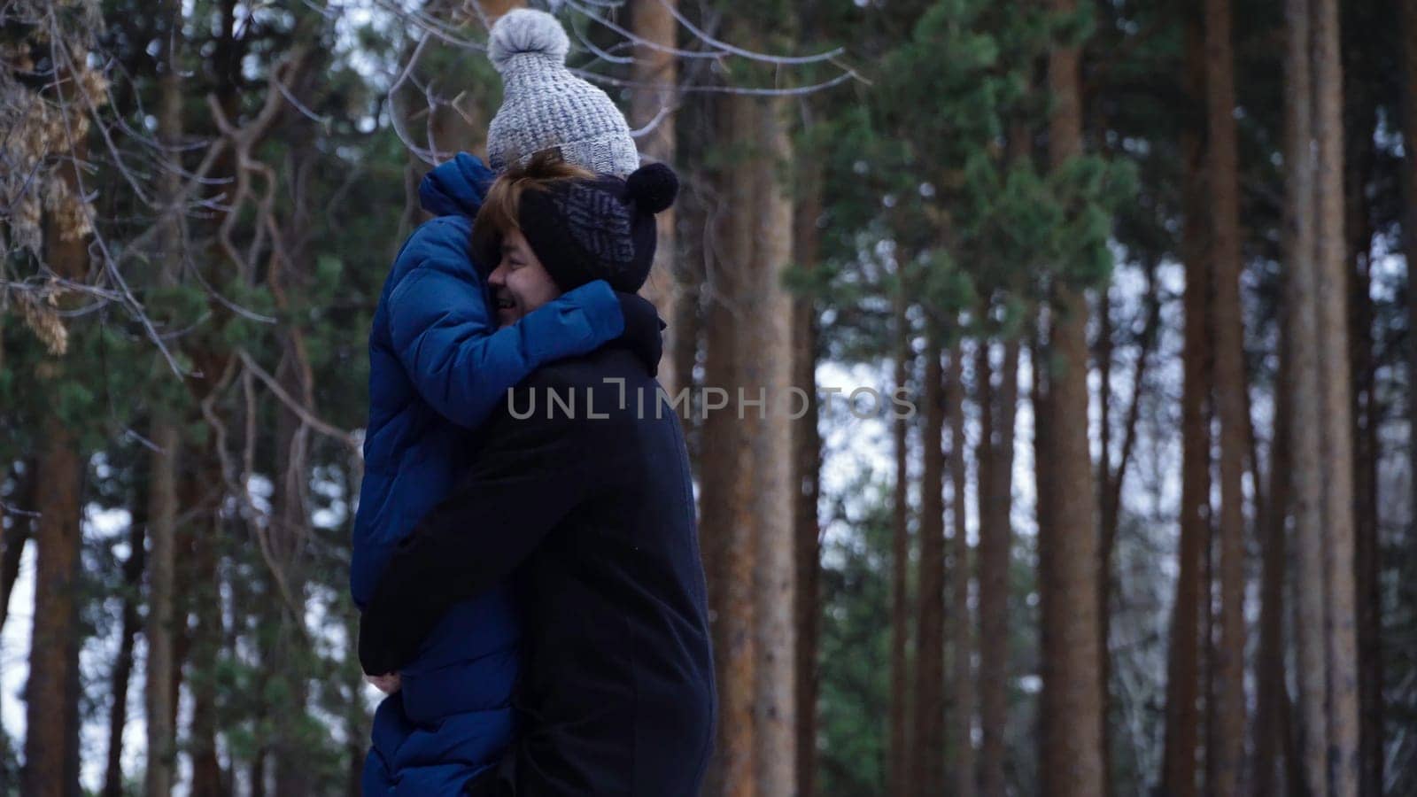 Young couple hugging and kissing in park in winter. Couple happy together. Young man circling his girlfriend in arms against winter forest.