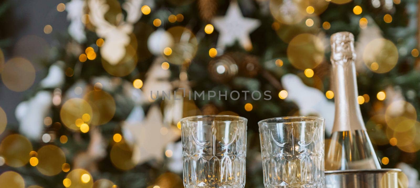 Champagne glasses, New Year decor. New Year's festive setting, family holidays.Two glasses of champagne are on the table against the background of New Year's decorated tree. by Matiunina