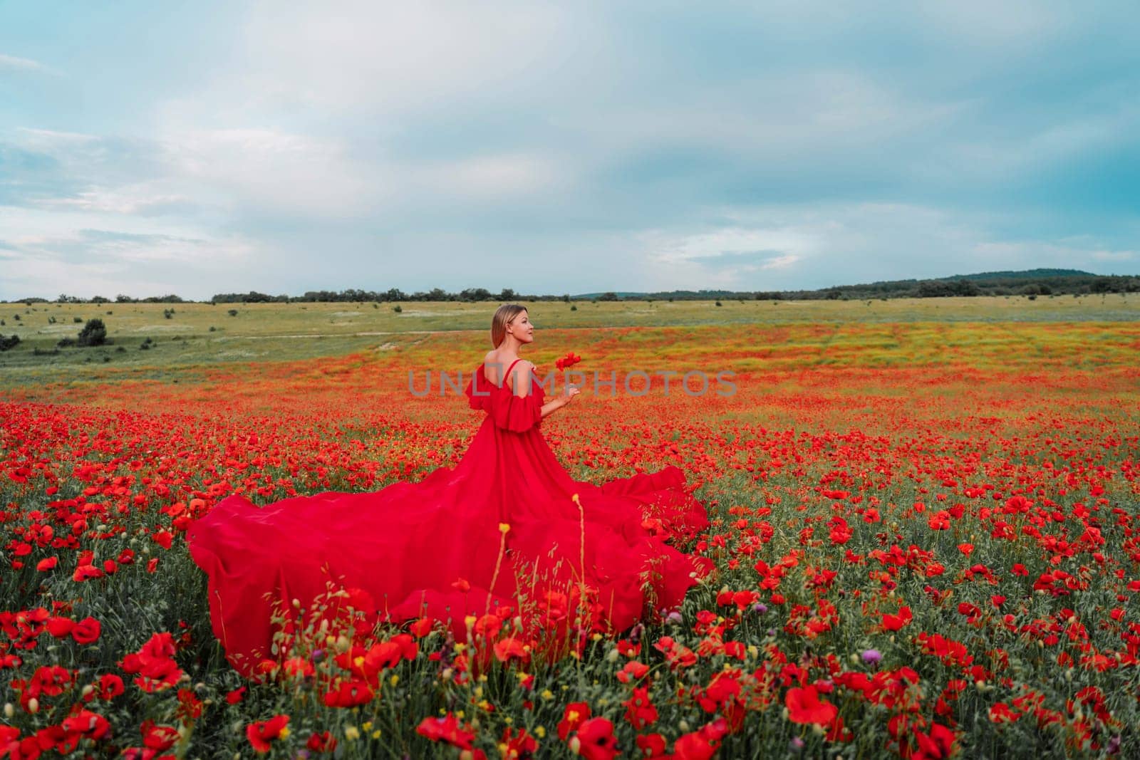 Woman poppy field red dress. Happy woman in a long red dress in a beautiful large poppy field. Blond stands with her back posing on a large field of red poppie