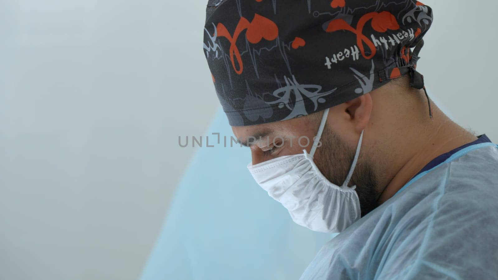 A close up male medical worker with a disposable mask and hat. Action. Surgeon at work in modern clinic
