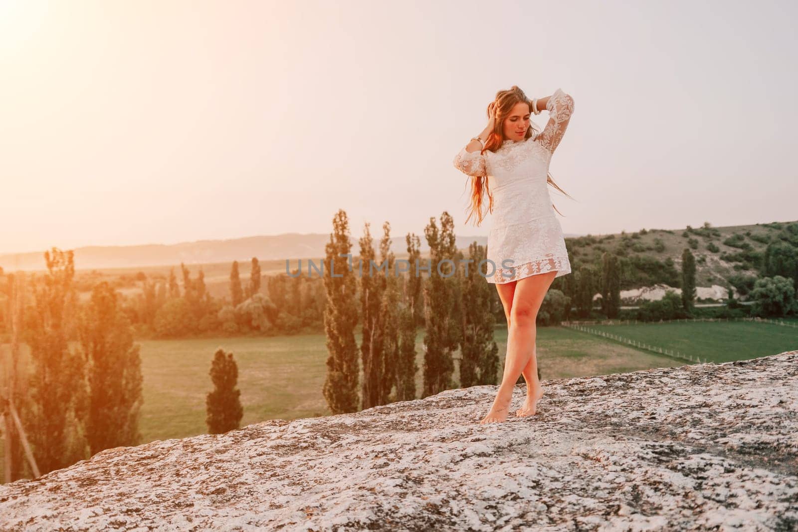 Romantic beautiful bride in white dress posing with sea and mountains in background. Stylish bride standing back on beautiful landscape of sea and mountains on sunset