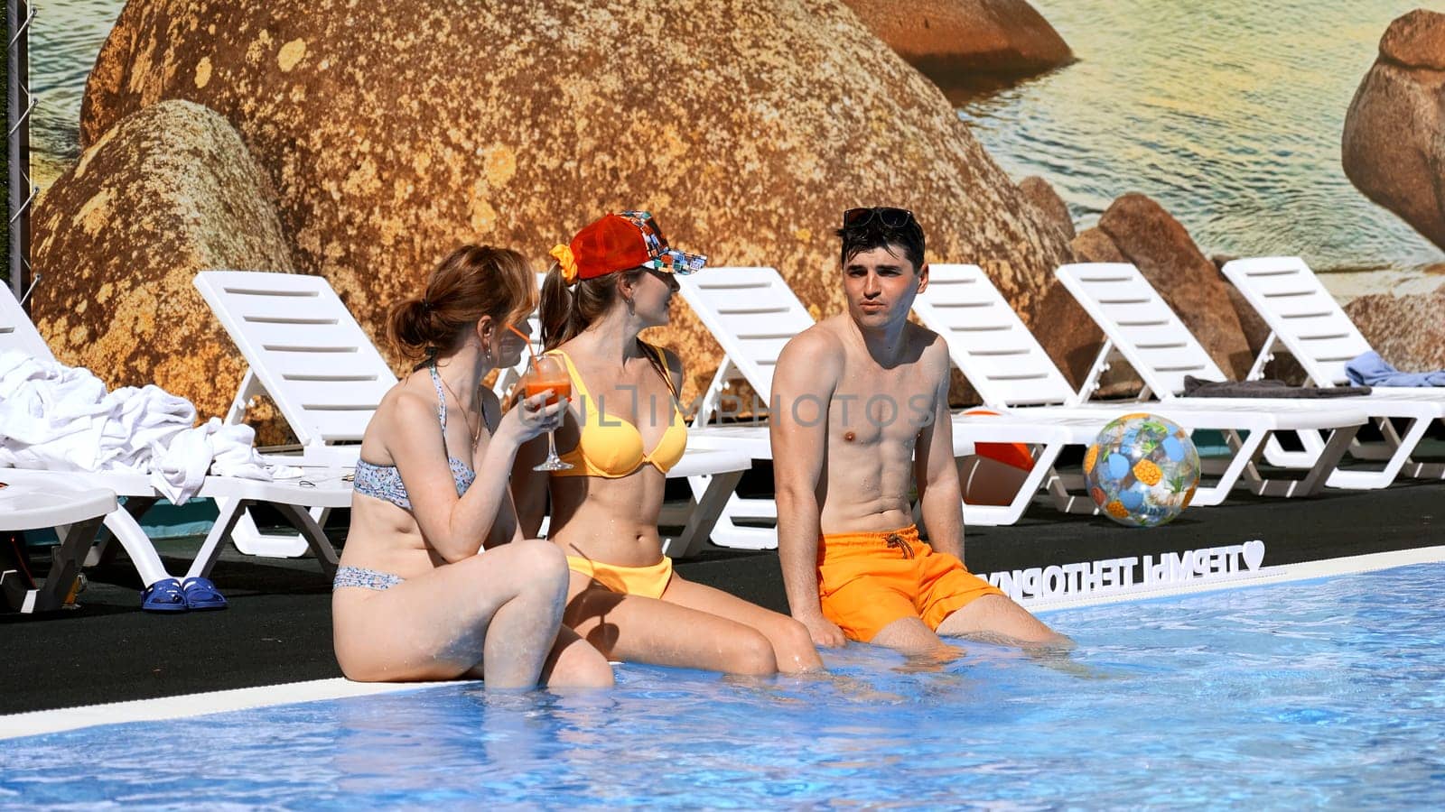 Two girls flirting with young man by the swimming pool. Clip. Concept of holiday romance