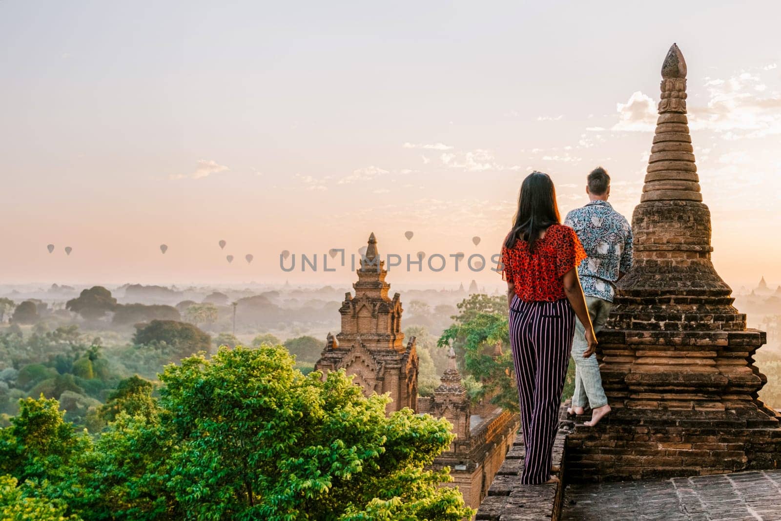 Bagan Myanmar, a couple of men and women are looking at the sunrise on top of an old pagoda temple. a couple watching sunrise with hot air balloons in the sky in Myanmar Asia Bagan