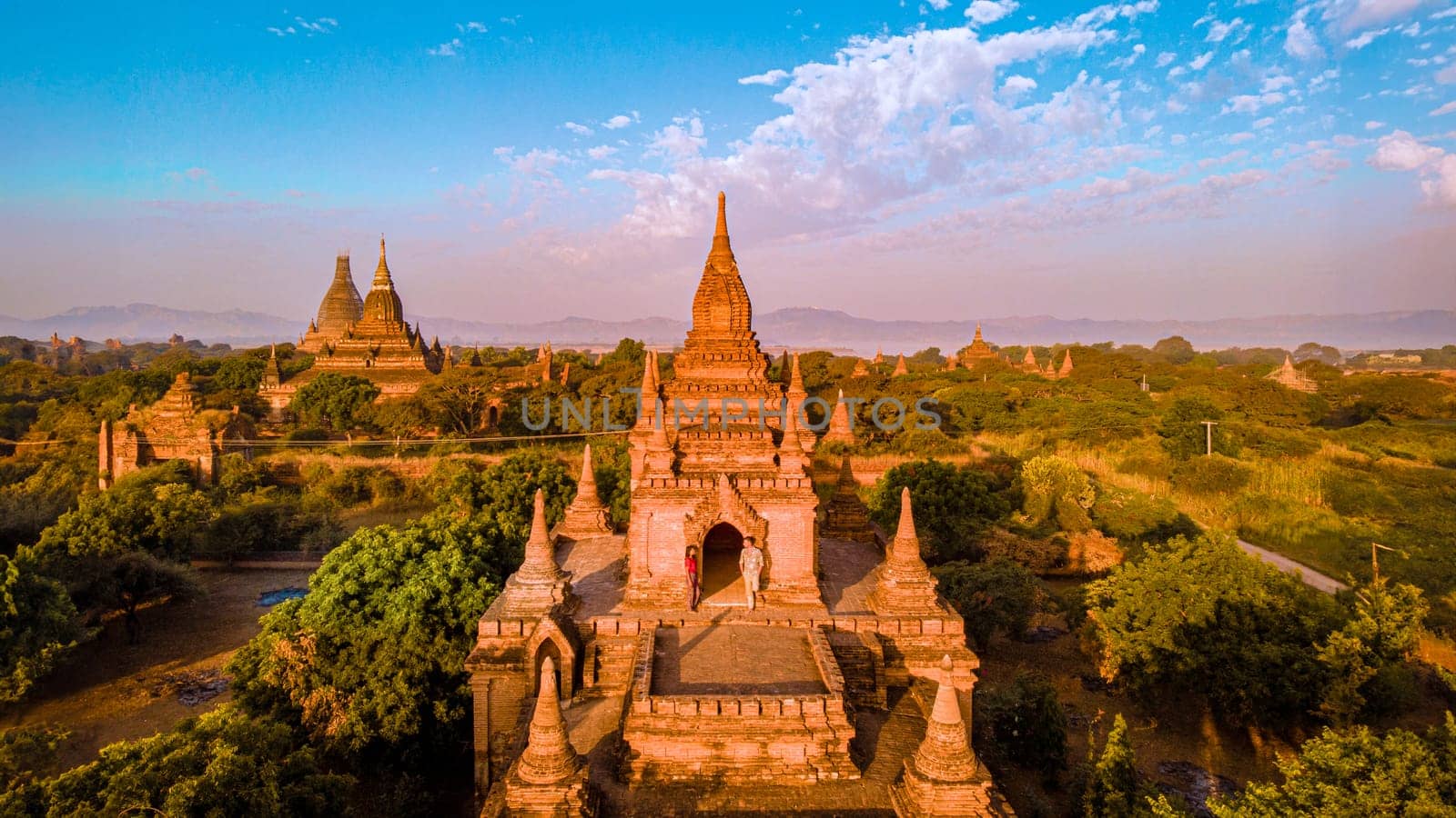 Bagan Myanmar, a couple of men and women are looking at the sunrise on top of an old pagoda temple.