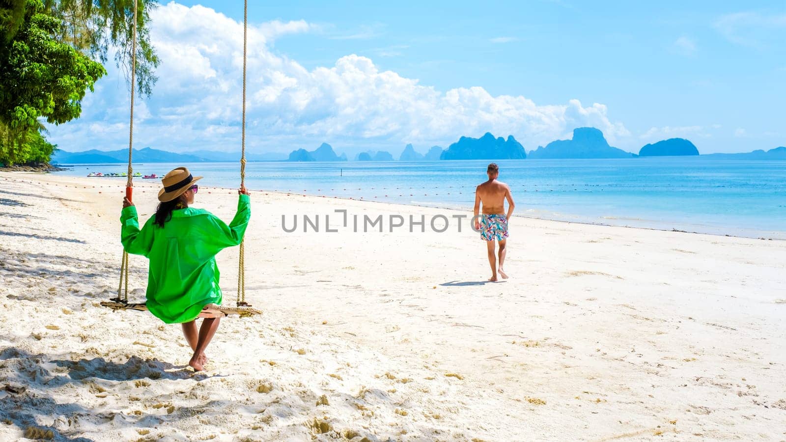 a mature couple of men and women on vacation in Phuket Thailand visiting the tropical beach, a couple on a swing under a tree on the beach in Thailand