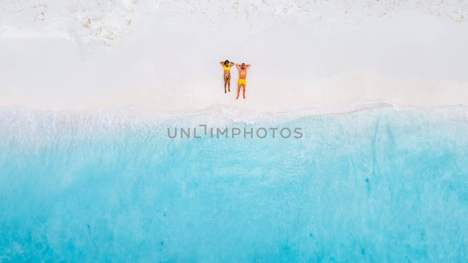 Drone top view of a couple of men and women lying down on the beach of Small Curacao Island, a couple relaxing on the beach of Curacao, top view at a tropical beach