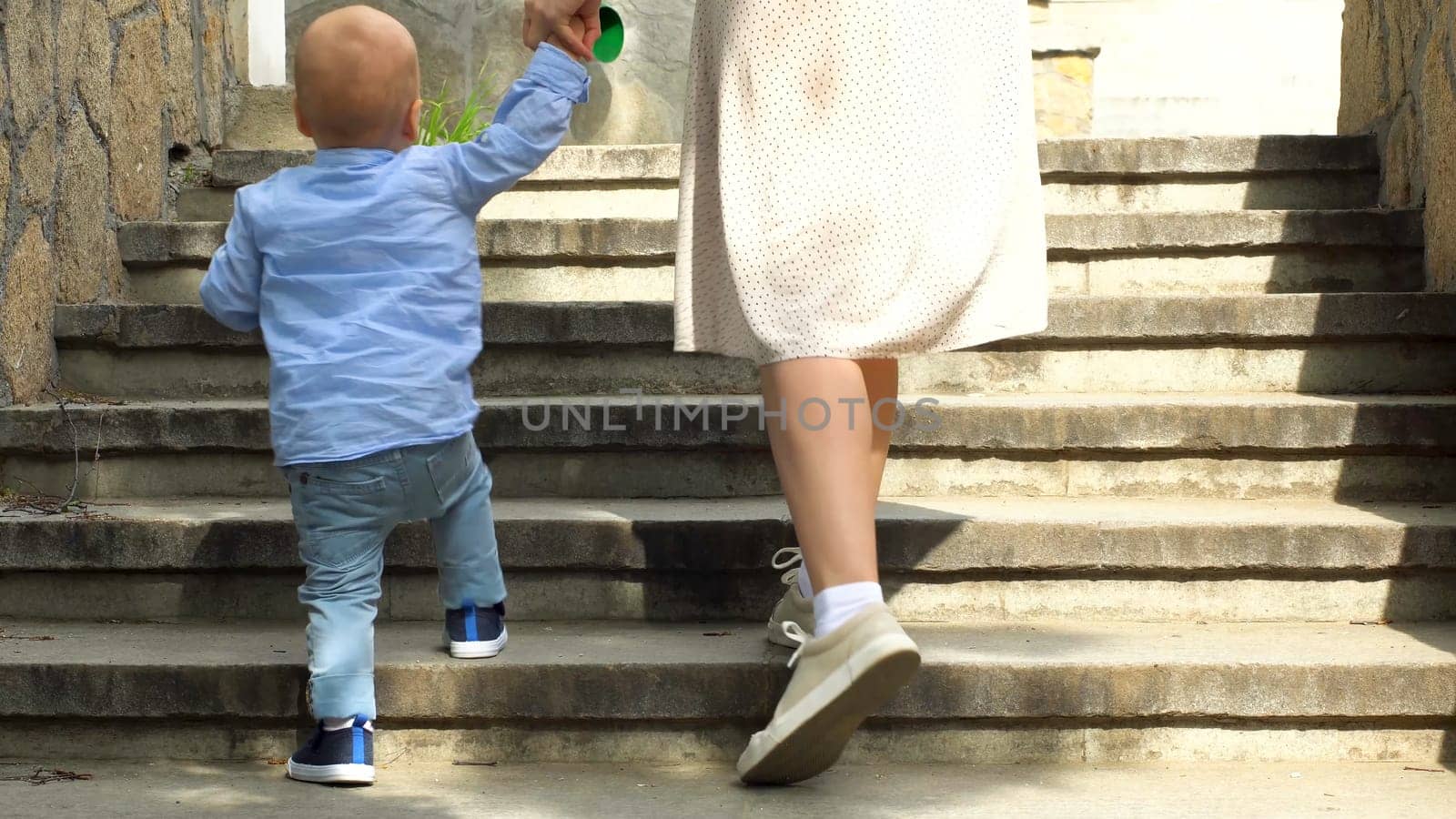 Close up of woman helping her little child boy to climb the stairs by holding his hand. Stock footage. Mother with small kid son walking up the stairs. by Mediawhalestock