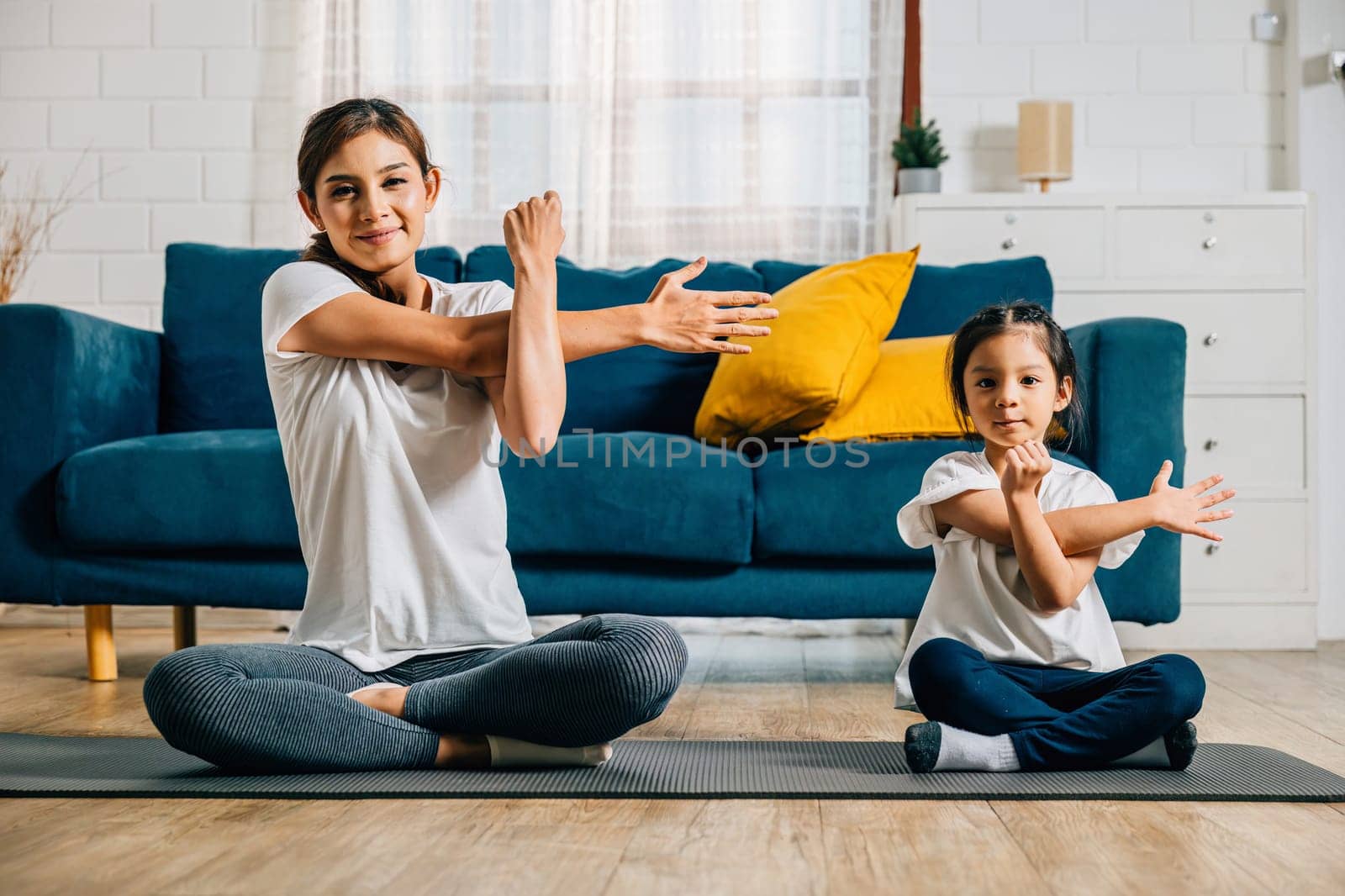 In the gym center a mother supports her daughter in stretching and yoga exercises by Sorapop