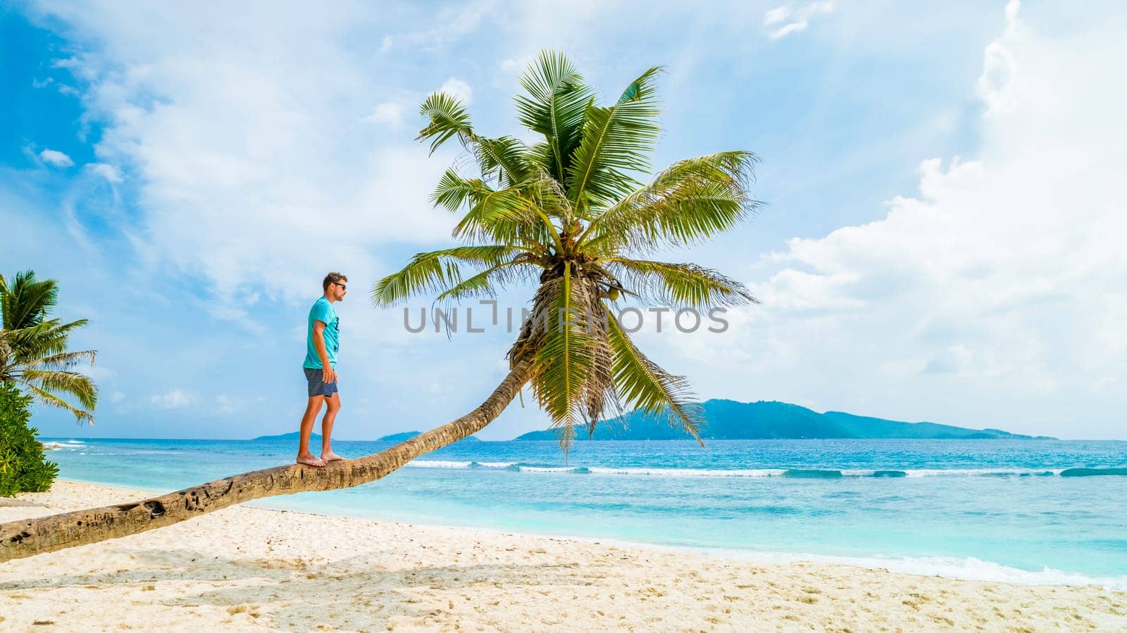 Young men relaxing at a palm tree on a tropical white beach at the La Digue Seychelles Islands by fokkebok