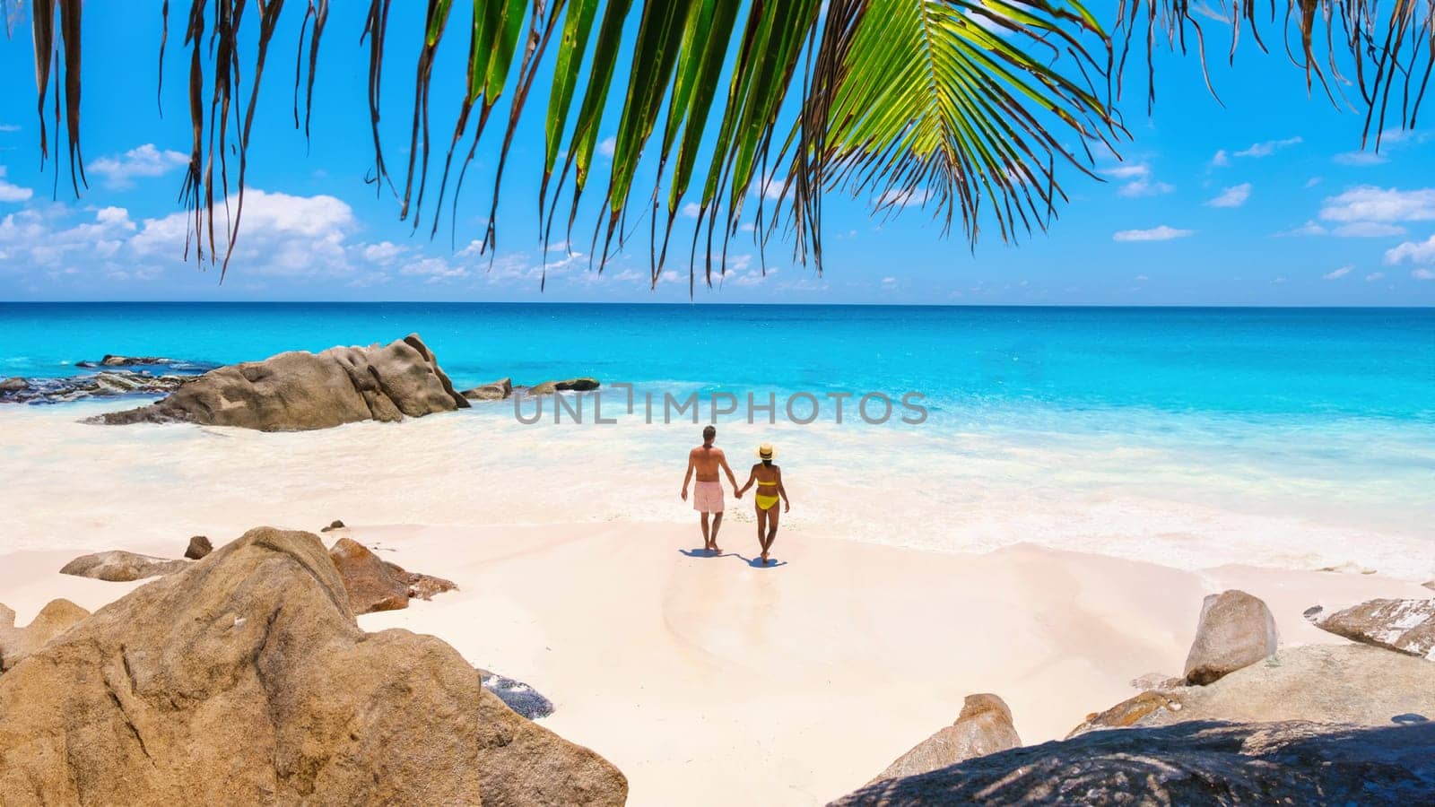 a mature couple of men and women on vacation in Seychelles visiting the tropical Beach of Anse Lazio Praslin Seychelles. couple walking at a tropical beach with palm tree leaves