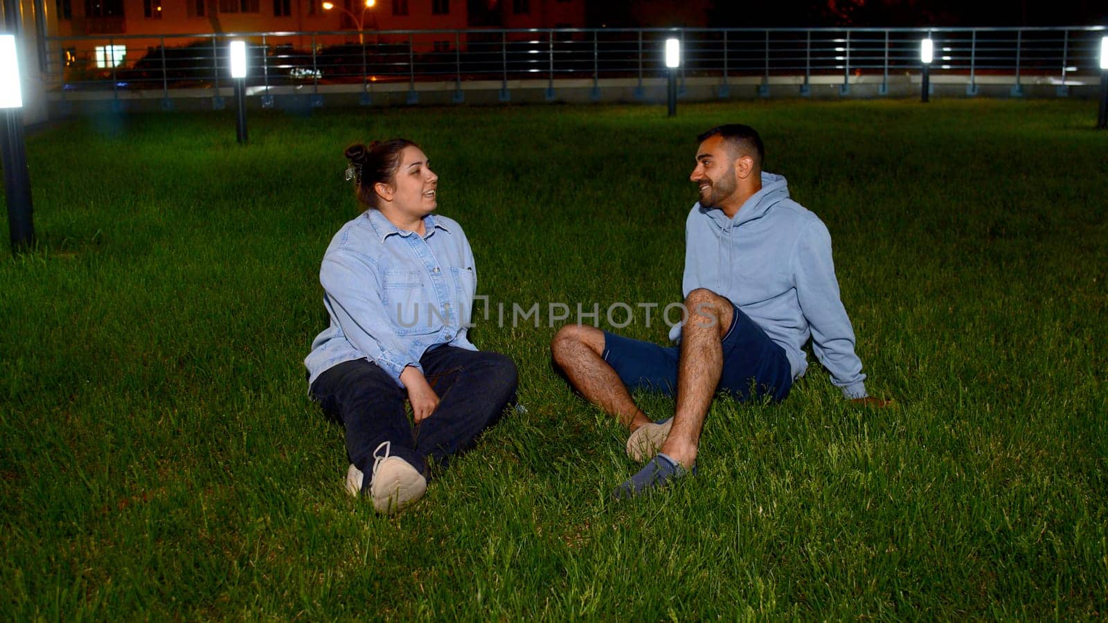 Romantic date within beautiful natural environment, green, juicy lawn. Media. Beautiful, young couple sitting on lush meadow and enjoying evening together