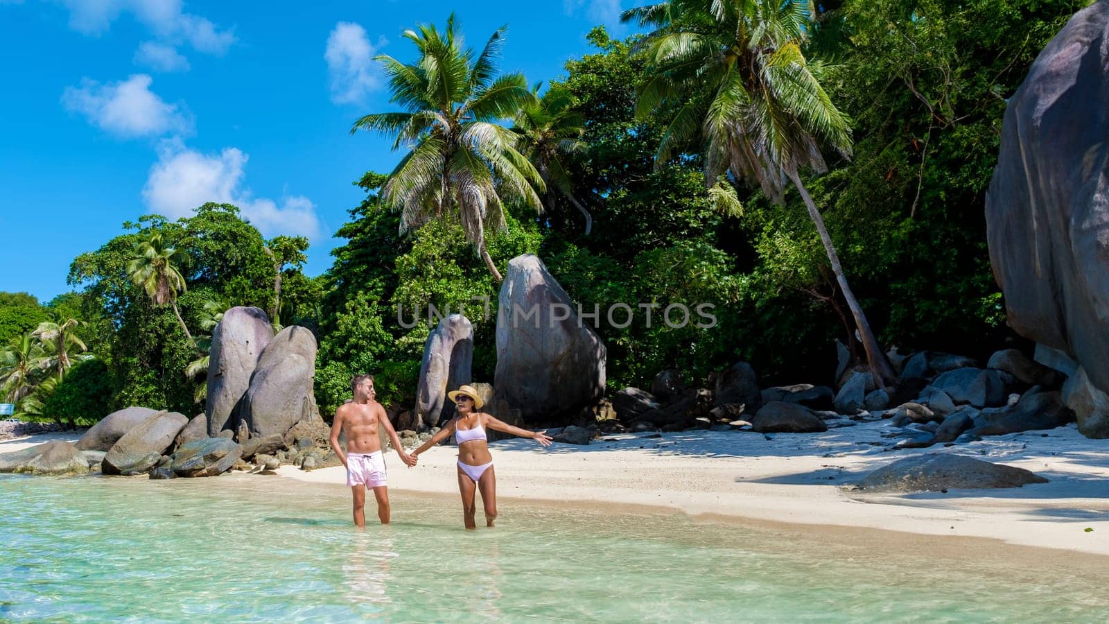 Mahe Seychelles tropical island with white sandy beaches and palm trees, a couple of men and women mid age on vacation at Seychelles visiting a tropical beach