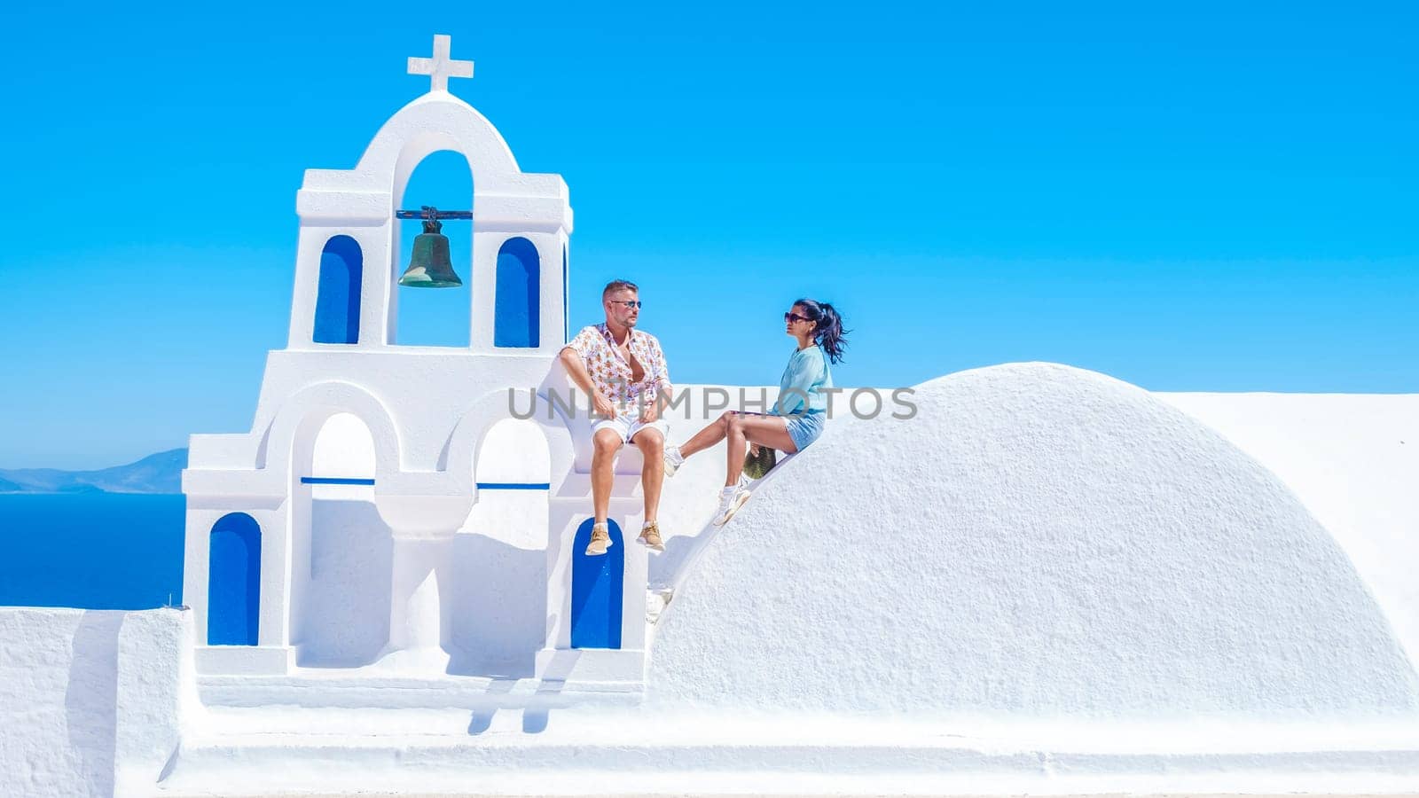 A couple watching the sunset on vacation in Santorini Greece, men and women visit the Greek village of Oia Santorini.