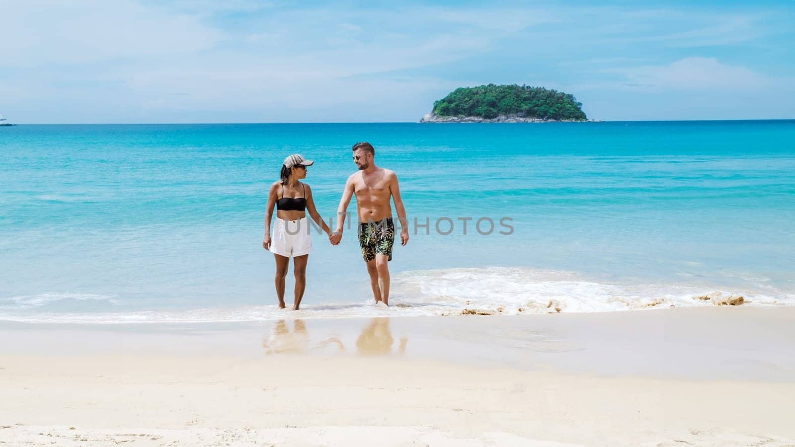Diverse couple walking on the beach of Kata Phuket Thailand during vacation, happy men and woman on vacation holidays in Thailand walking by the ocean of Kata Beach Phuket