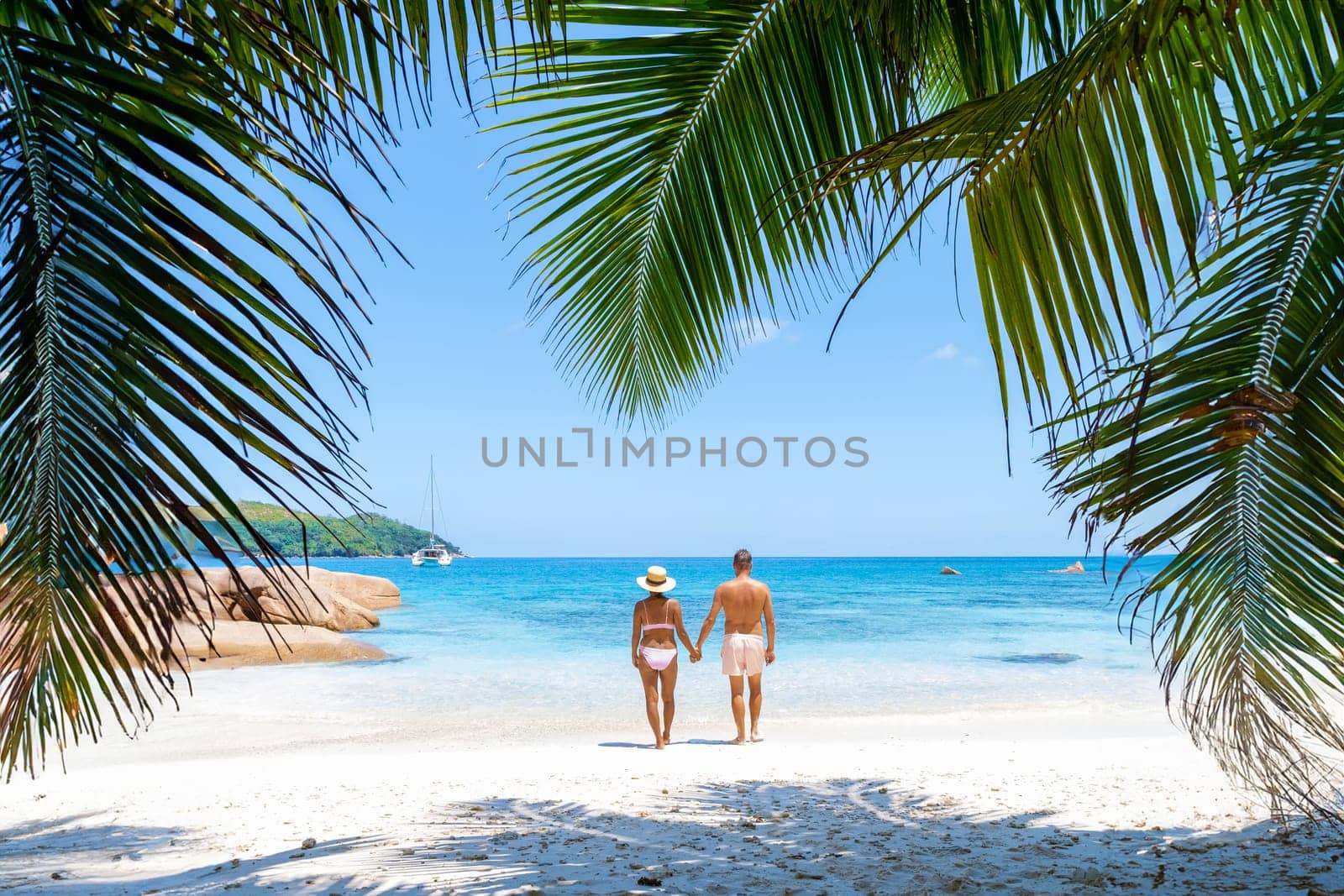 a mature couple of men and women on vacation in Seychelles visiting the tropical beach of Anse Lazio Praslin Seychelles. beautiful beach with palm leaves