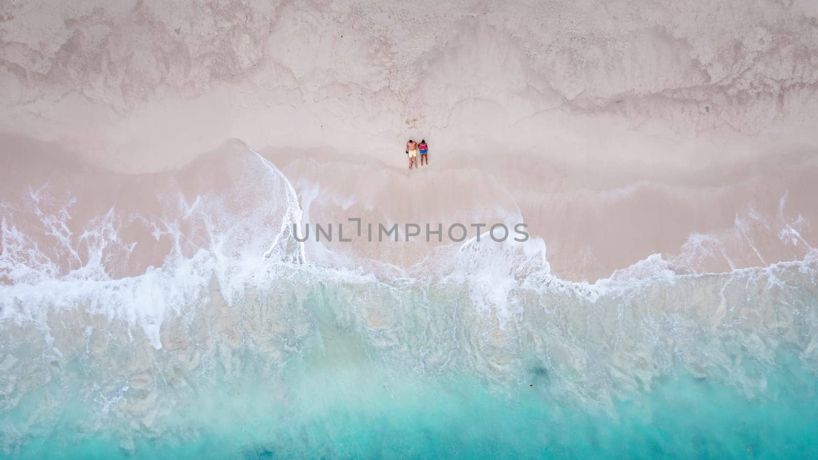 Drone aerial view at a couple on the beach at Freedom Beach in Phuket Thailand during vacation, top view at tropical beach with people on the beach from above in Thailand