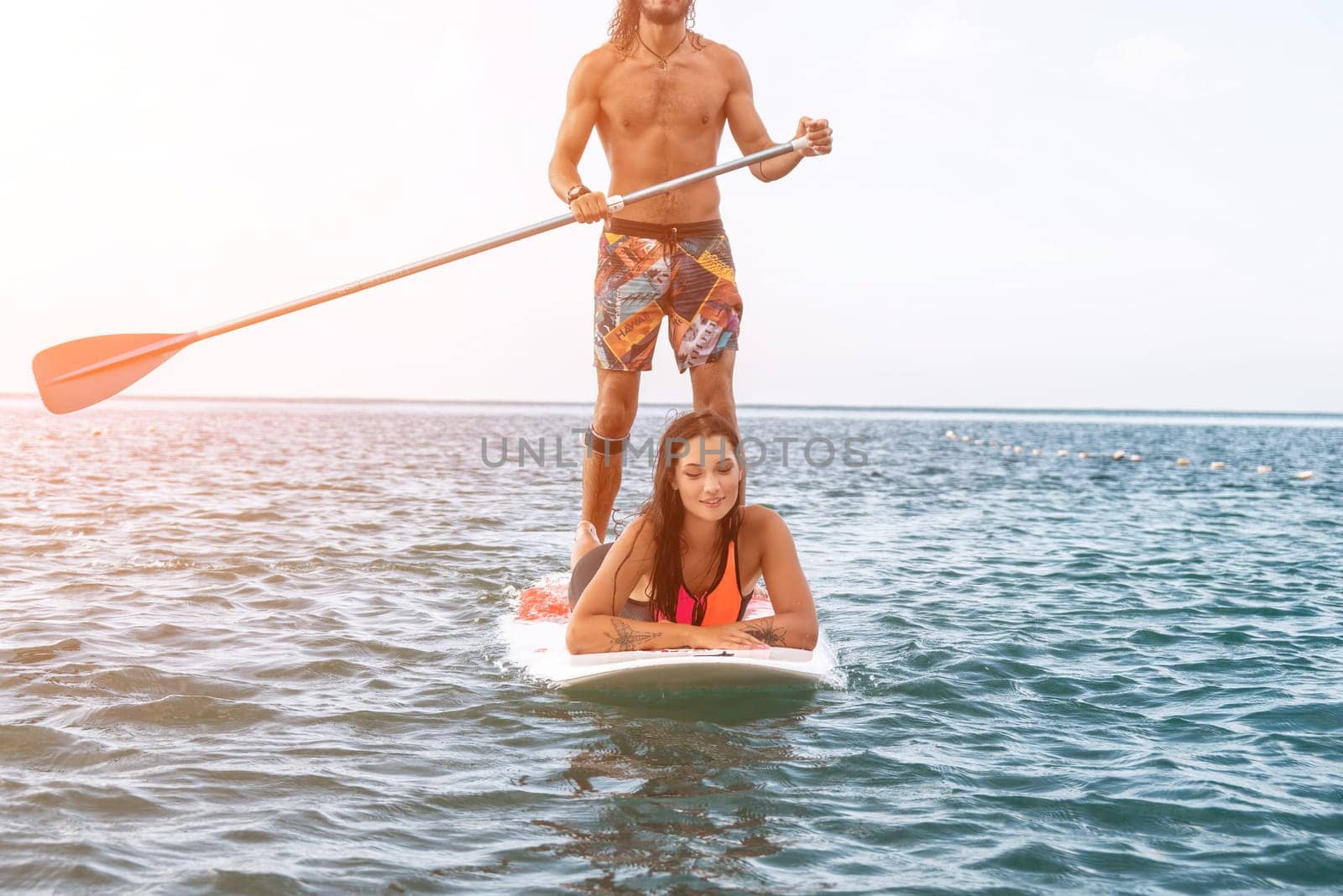 Sea woman and man on sup. Silhouette of happy young woman and man, surfing on SUP board, confident paddling through water surface. Idyllic sunset. Active lifestyle at sea or river