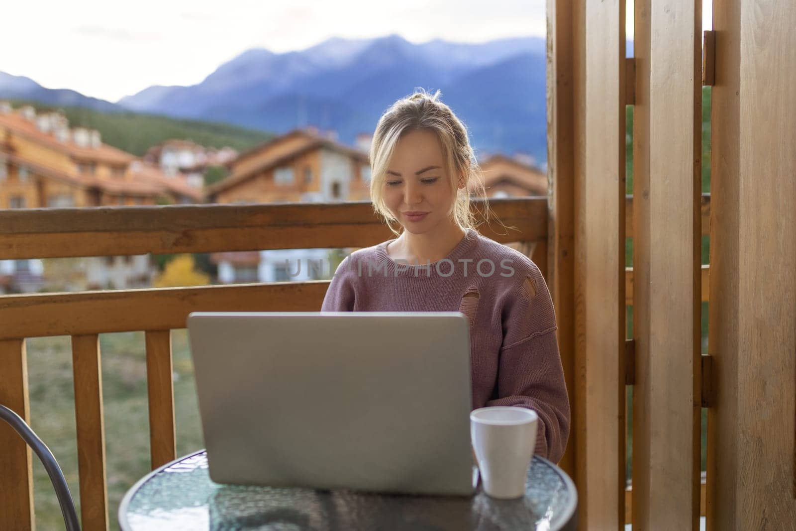 Girl working with a great view mountains. Workplace in country in backyard house in morning. Woman remote work on laptop while sitting at a table outdoors. Concept freelance lifestyle. Internet 5G