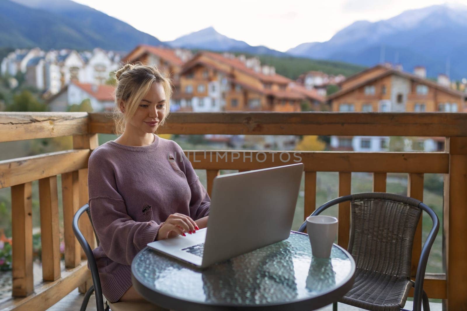 Girl working with a great view mountains. Workplace in country in backyard house in morning. Woman remote work on laptop while sitting at a table outdoors. Concept freelance lifestyle. Internet 5G