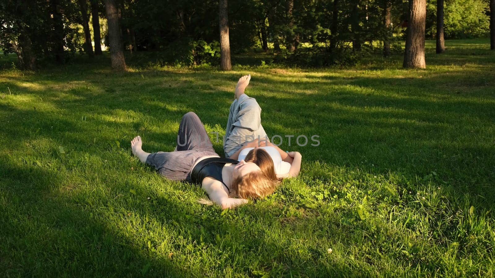 Friends are lying on green grass in park on sunny summer day. Concept. Beautiful girlfriends are lying on green grass in park. Relaxing in park on grass.