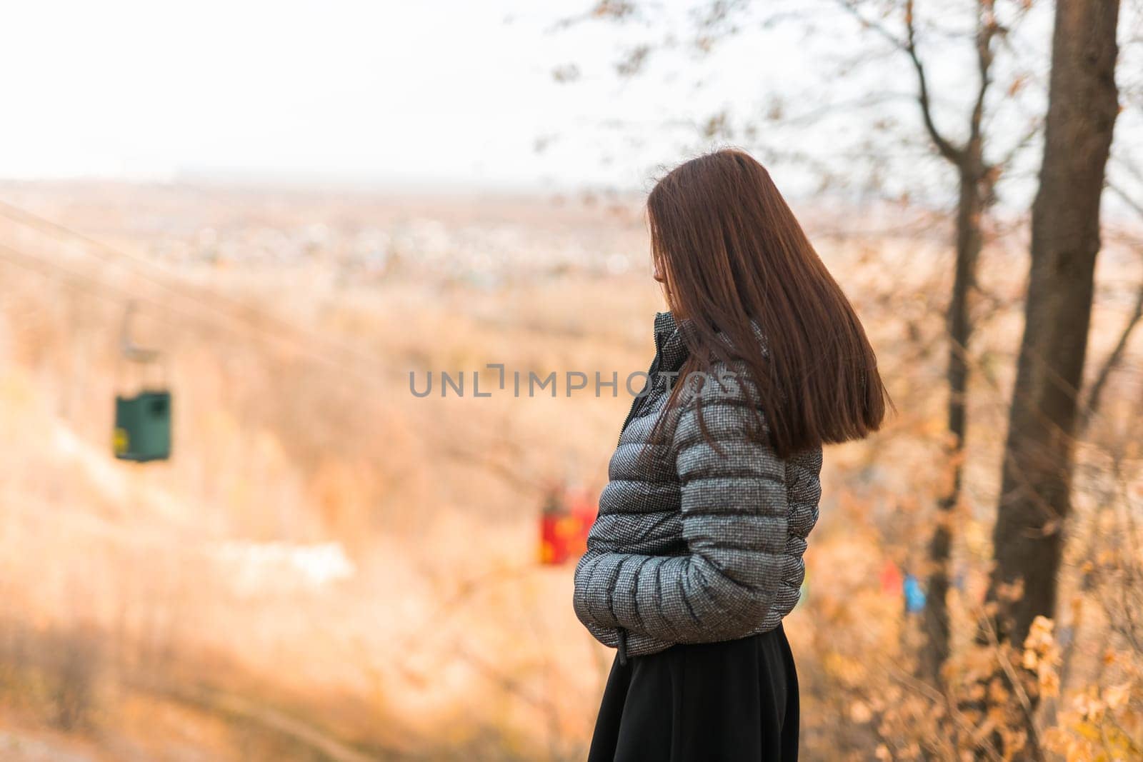 Girl in fall park against background of cable car copy space. Woman with long curly hair. Beautiful sunlight in the forest. Hair care. Generation Z gen z and youth. by Satura86