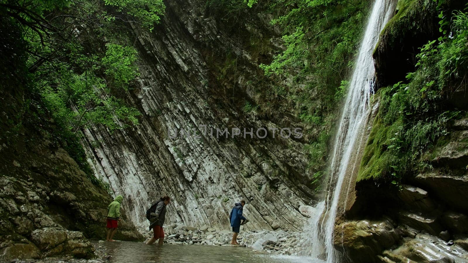 Jungle waterfall with walking in water. Creative. Concept of hiking, summer trip in wild nature. by Mediawhalestock