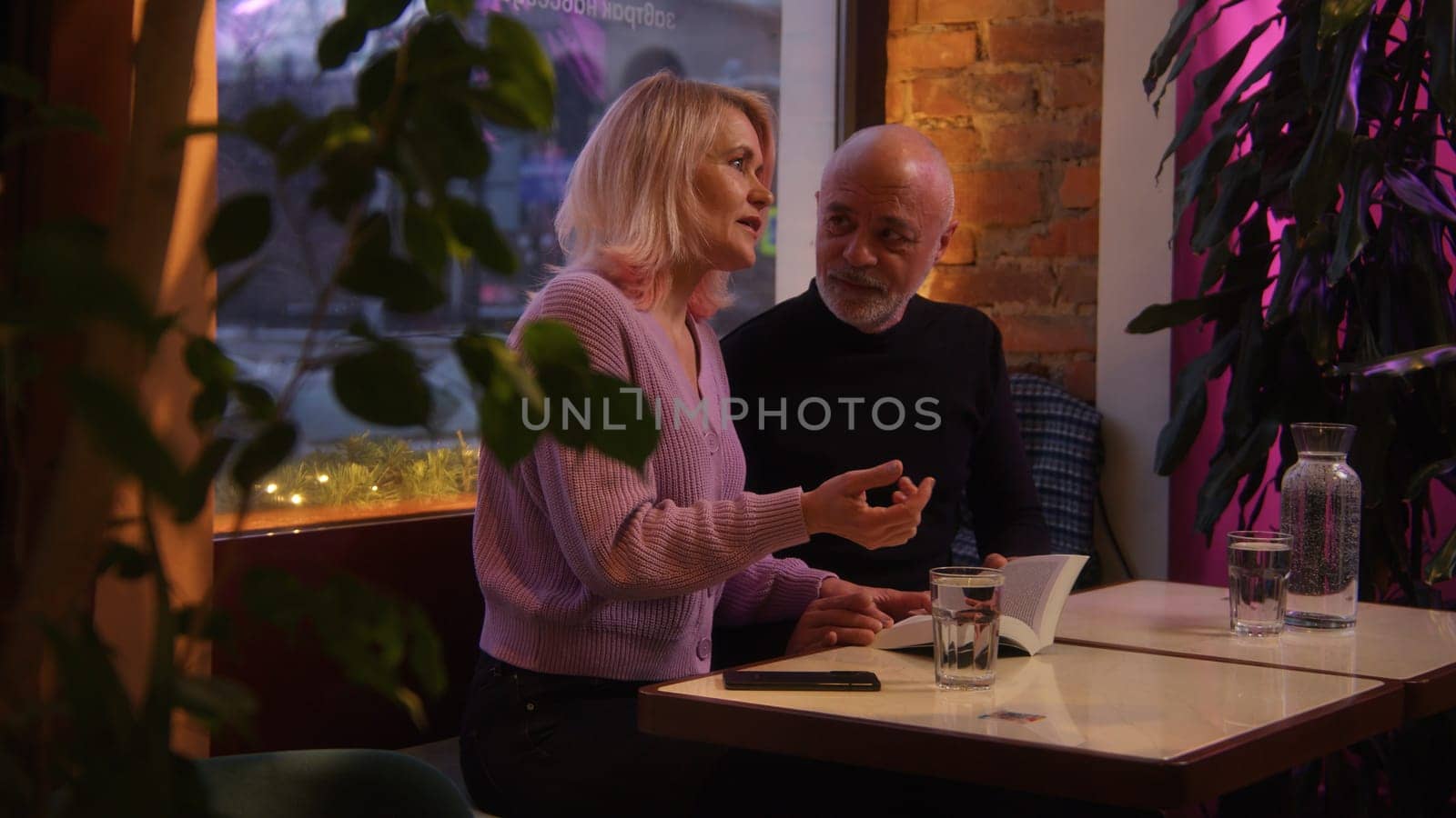Elderly woman and man communicate in cafe. Stock footage. Beautiful elderly couple is having date in cafe. Evening date of elderly couple in cafe.