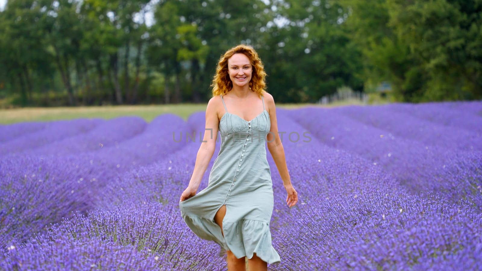Young woman in a blue dress walking through lavender field. Action. Beautiful girl in Provence, France. by Mediawhalestock