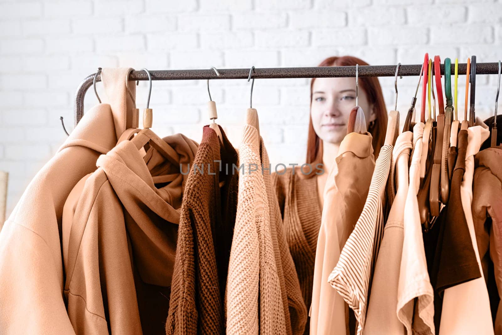 Color of the year 2024: Peach Fuzz. beautiful young woman in beige coat standing in front of hanger rack and choosing outfit dressing. Selection of a wardrobe, stylist, shopping. Clothes designing