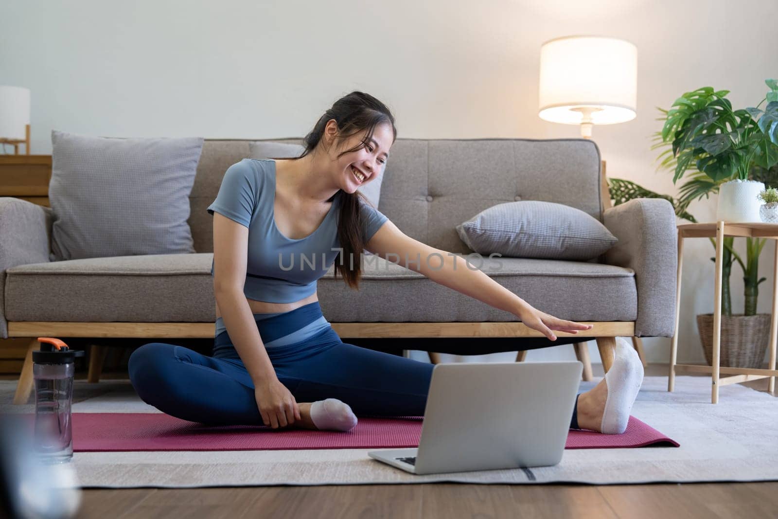 Young Asian sporty fitness woman coach do practice video online training yoga laptop in living room at home.