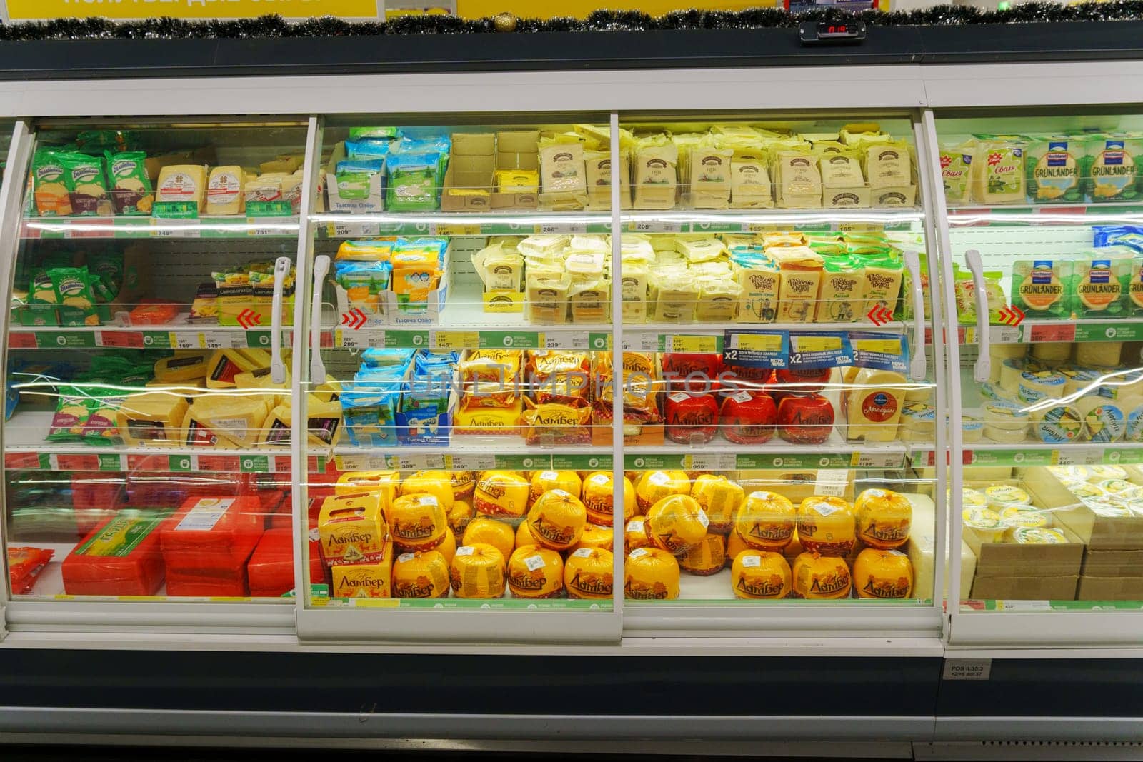 Tyumen, Russia-December 11, 2023: Glass fridge with various dairy products cheese in grocery store.