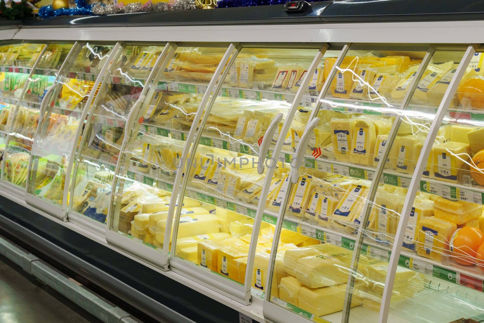 Tyumen, Russia-December 11, 2023: Glass fridge with various dairy products cheese in grocery store. by darksoul72