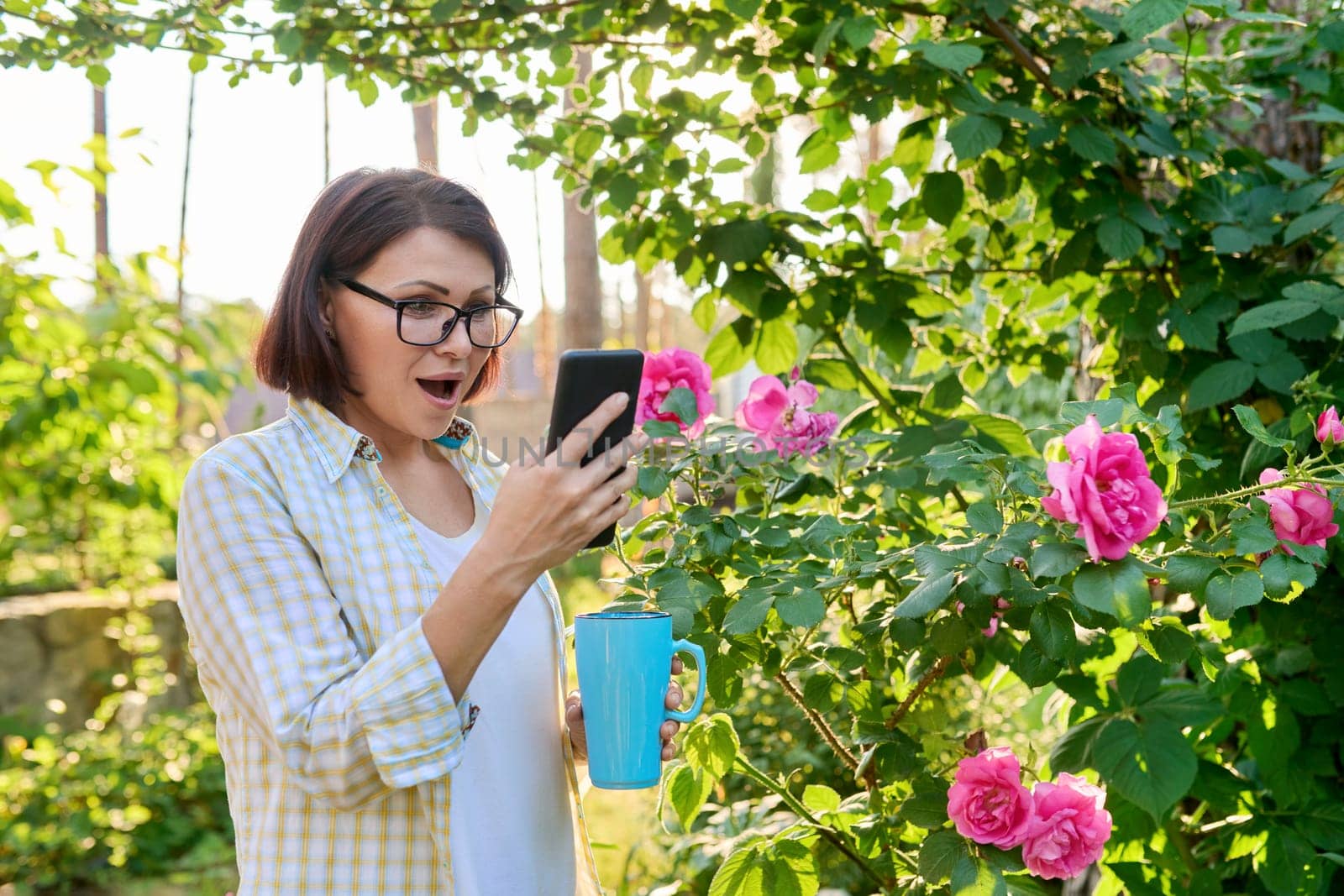 Mature woman resting in backyard using smartphone for video call by VH-studio