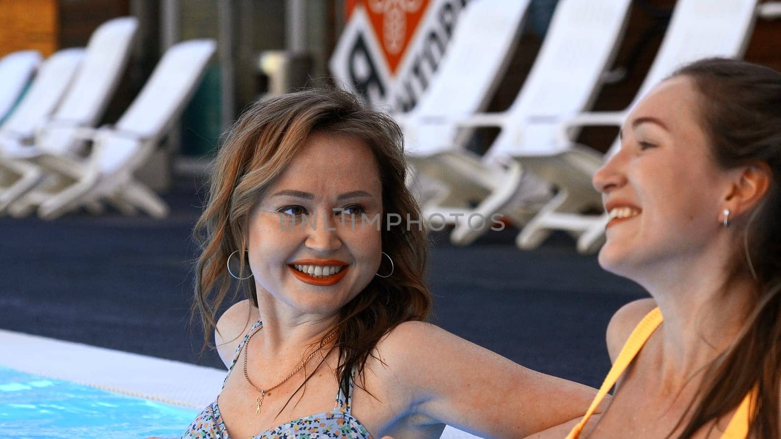 Young caucasian girls relaxing by the hotel pool. Clip. Adult women gossiping and smiling during vacation