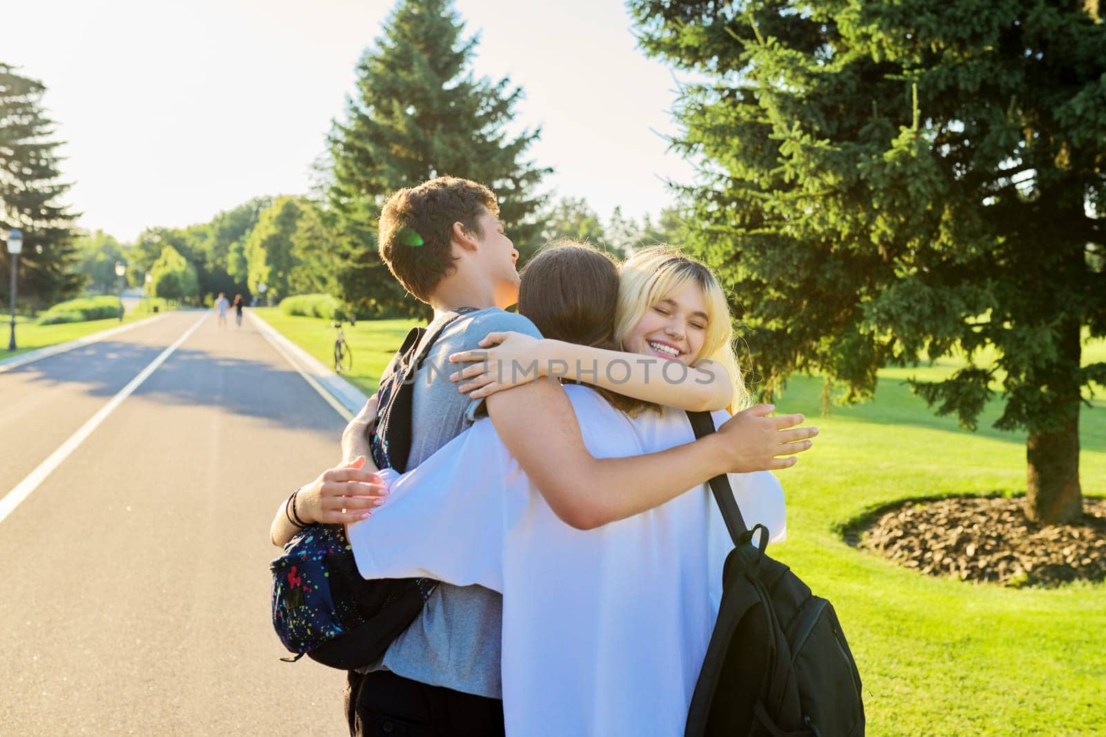 Happy teenage friends hugging together on sunny day in park. Group of teenagers together, back view. Friendship, adolescence, summer, vacation, lifestyle, fun, happiness, holiday, leisure people