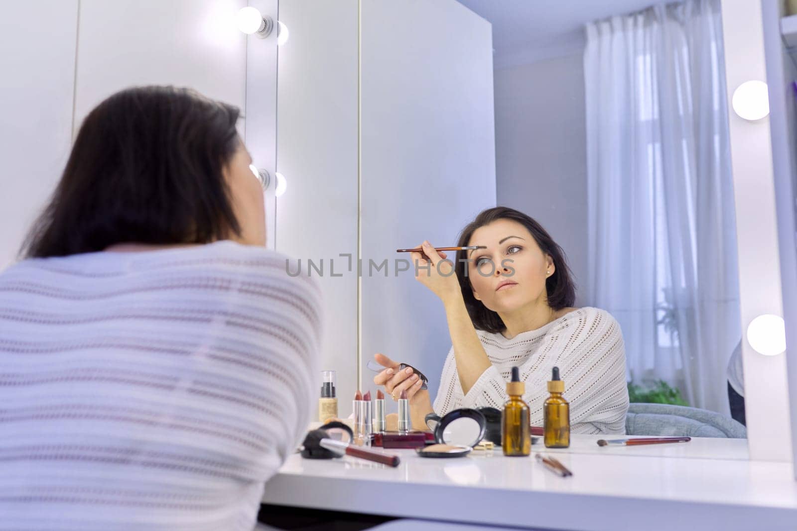 Beautiful middle aged woman doing makeup in front of a mirror. Cosmetics, beauty, make-up, face care, skin care, women 40s age concept