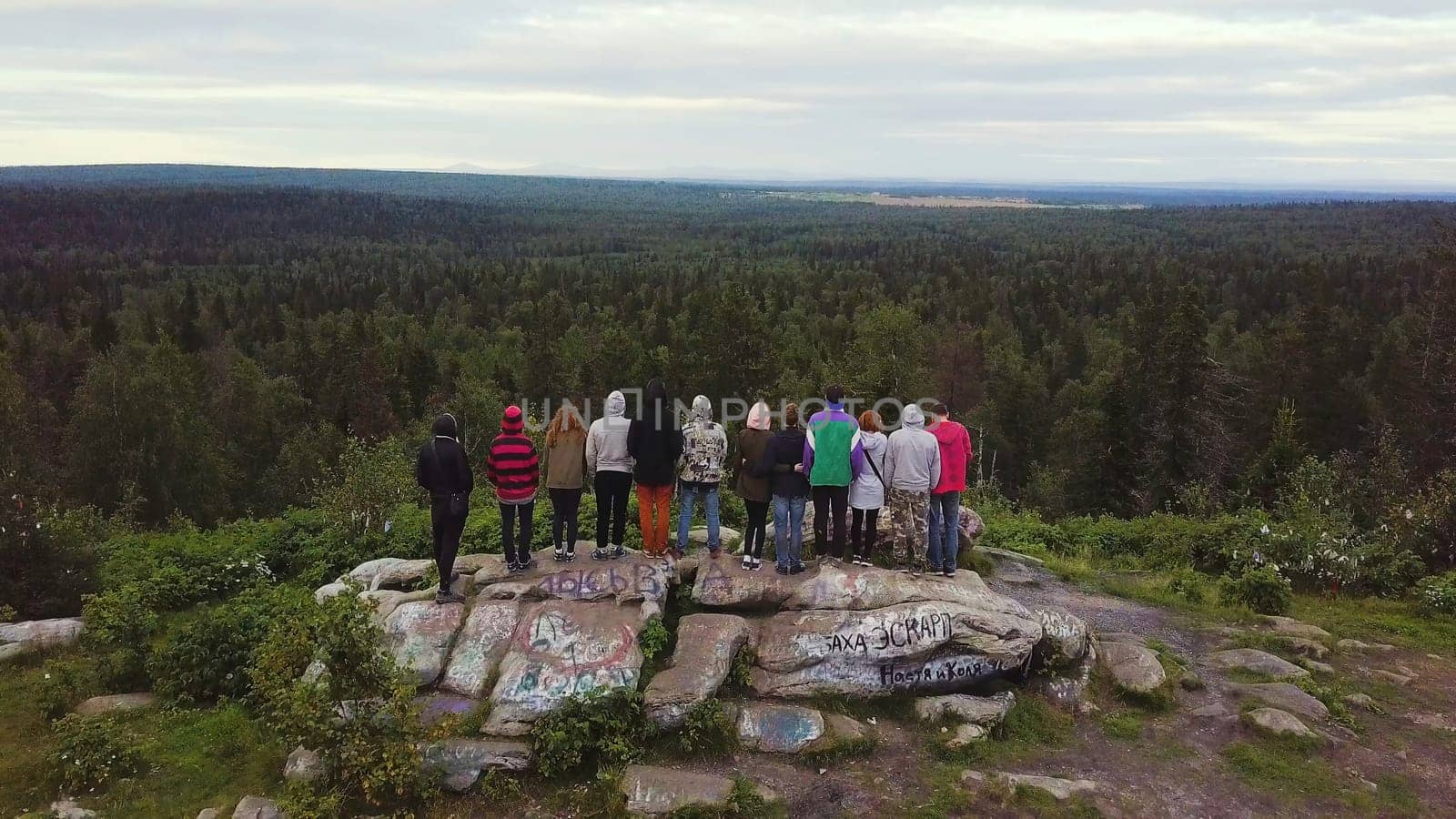 People holding hands stand on top of the mountain and look into the distancewith nature background with forest. Rear view on the people in the campaign standing on the edge of the mountain holding hands, aerial view. Beautiful landscape with forest and mountains by Mediawhalestock