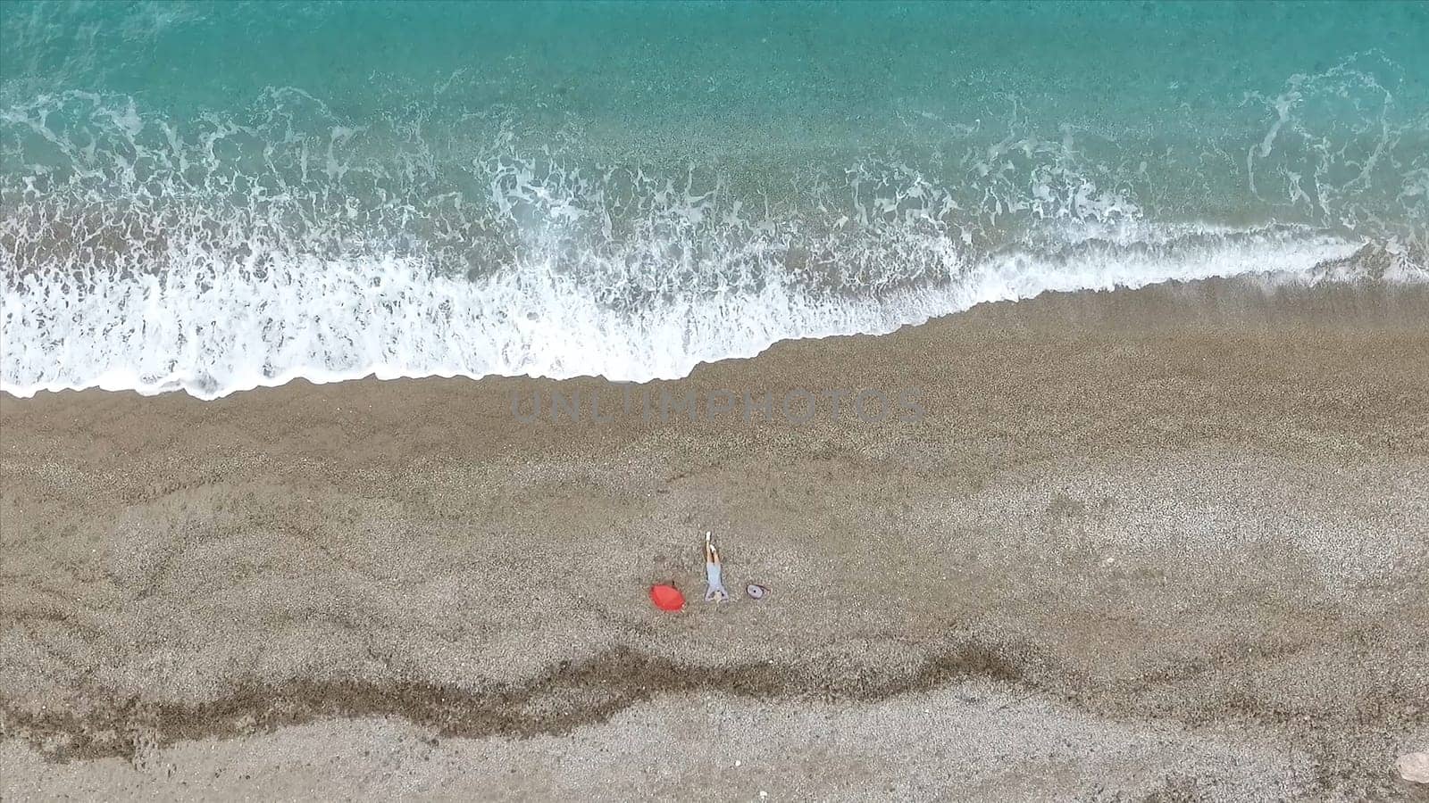 Young woman lying on the back near the waves of blue sea. Footage. Top view.