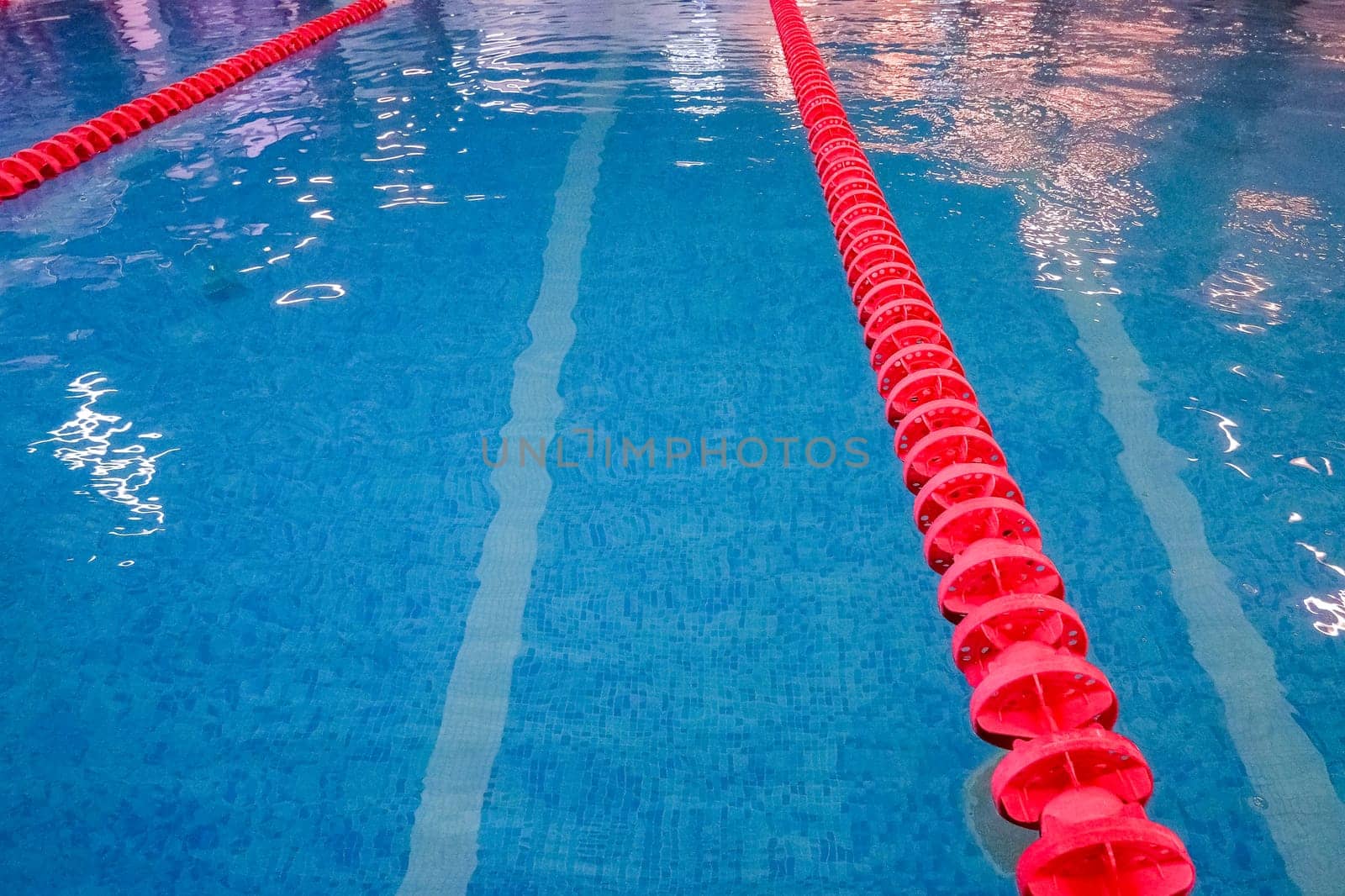 empty swimming pool with many lanes.An empty sports pool with a red dividing path. Blue water. Selective focus.Track and lanes of a competition swimming pool by YuliaYaspe1979