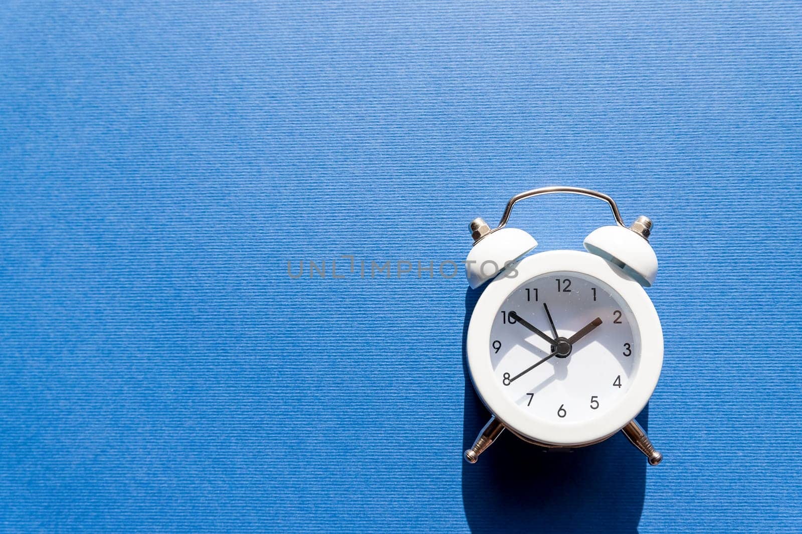 Small white retro clock isolated on blue background.Free time concept. Copy space.Time management, punctuality, awakening concept.time limit, date, timeline for compliance. by YuliaYaspe1979