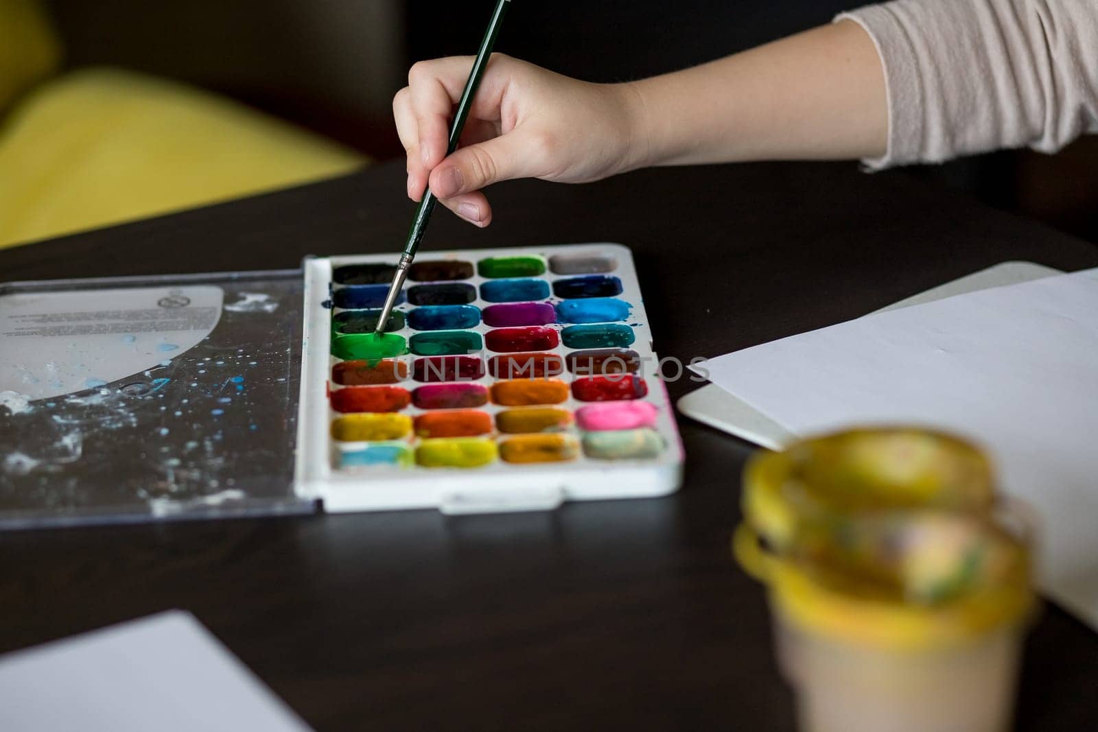 Choosing colors for first drawing - close-up of paint buckets with kids hand and paintbrush