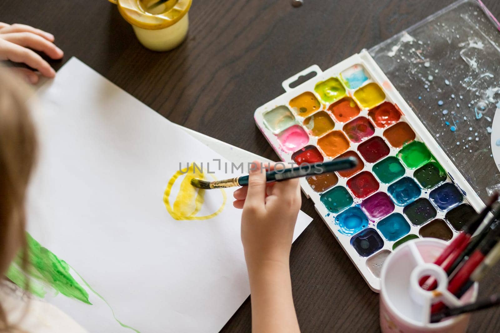 Choosing colors for first drawing - close-up of paint buckets with kids hand and paintbrush