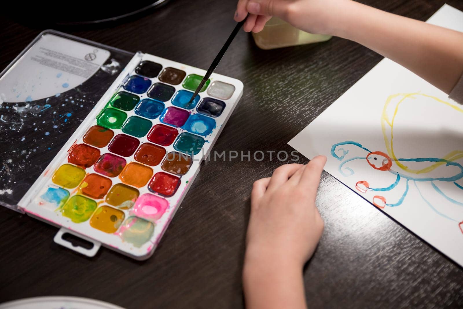 Child holding brush and painting on white paper.Choosing colors for drawing.Watercolor paints and brushes for painting. Children's creativity, painting, early development. by YuliaYaspe1979