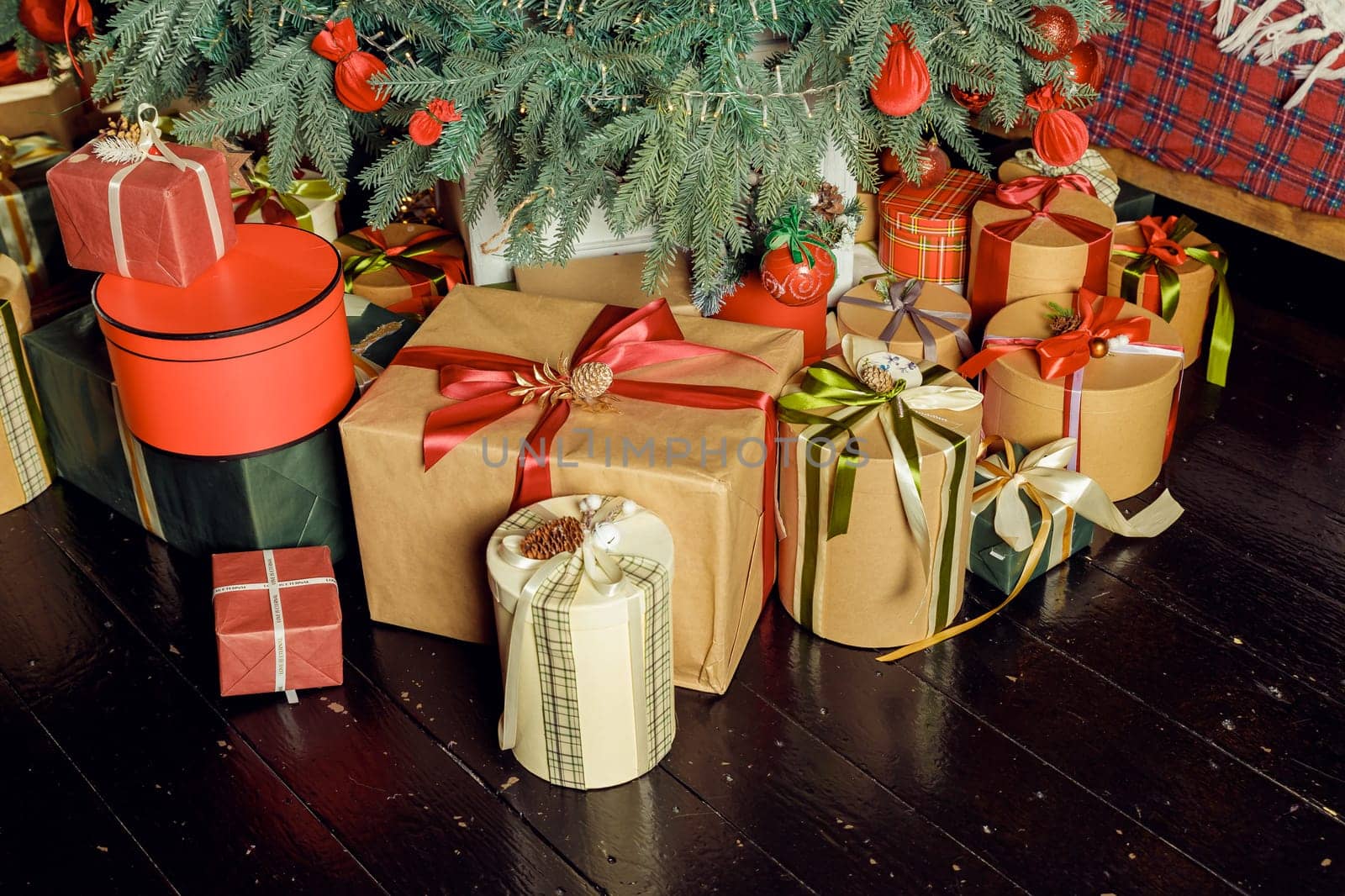 Christmas background with red gift boxes decorated with golden ribbon on floor and child toys under Christmas tree, copy space. Winter holidays concept