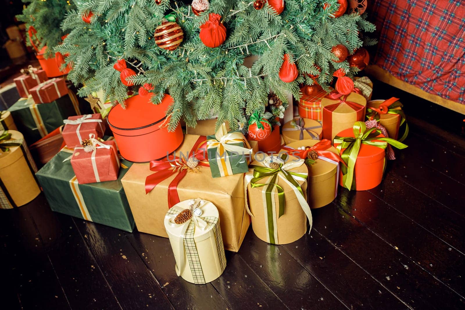 Christmas background with red gift boxes decorated with golden ribbon on floor and child toys under Christmas tree, copy space. Winter holidays concept