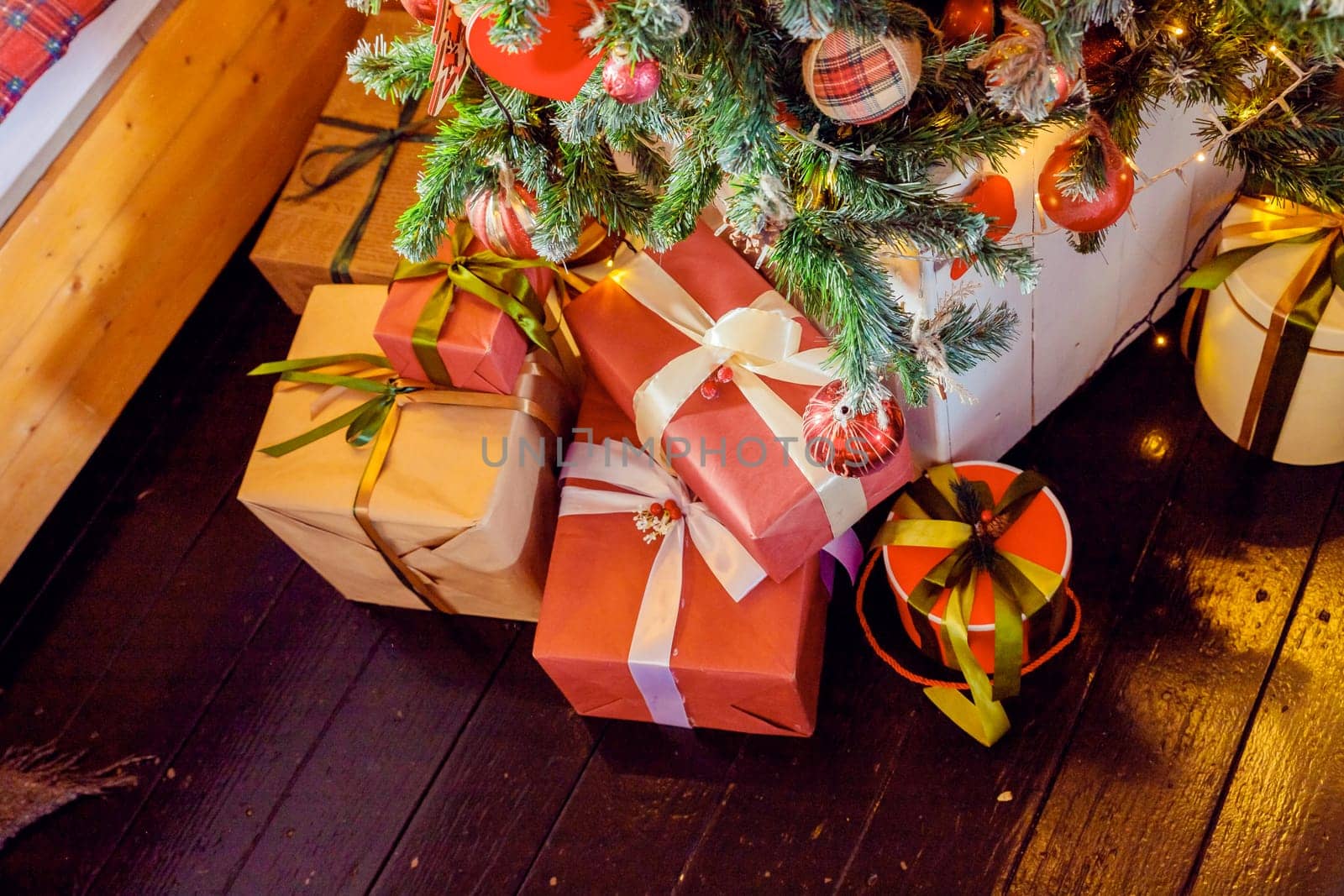 Christmas background with red gift boxes decorated with golden ribbon on floor and child toys under Christmas tree, copy space. Winter holidays concept