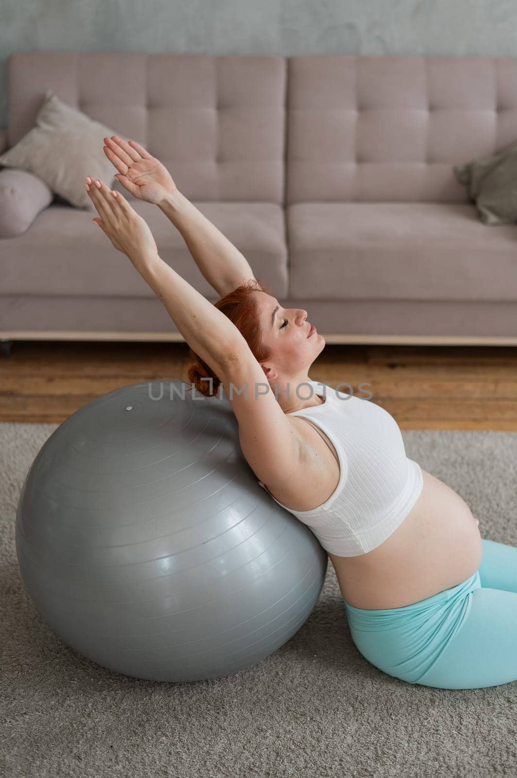 Pregnant red-haired woman doing exercises on fitness ball at home