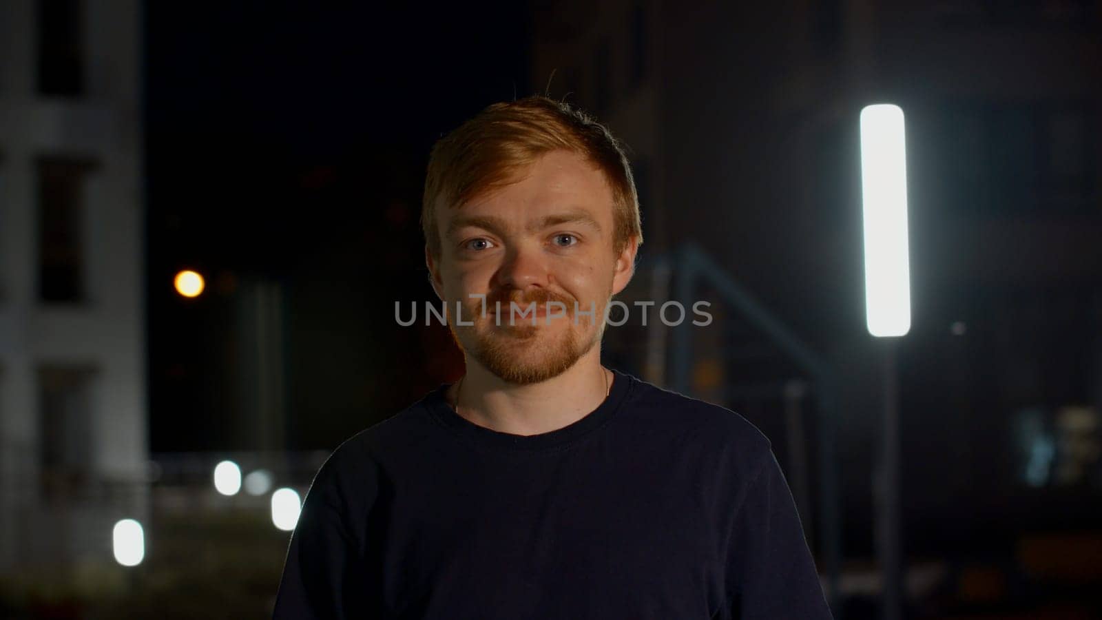 A handsome man posing on the street. Media. Night shooting of a portrait of a man with a beard in a hat. High quality 4k footage