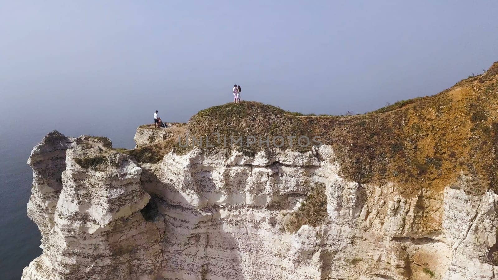 Couple traveling together on white cliff edge on blue sky background, lifestyle concept. Young couple of travelers on a hill with stunning views of the ocean.